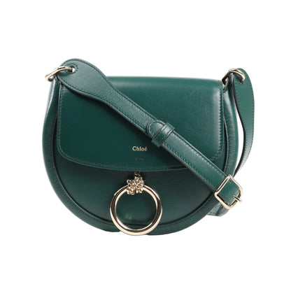 Front view of a Chloé Arlène shoulder bag in smooth green leather featuring a saddle-shaped body, flap closure, adjustable shoulder strap, and gold-tone ring with lion charm.