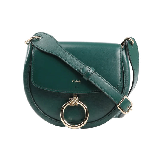 Front view of a Chloé Arlène shoulder bag in smooth green leather featuring a saddle-shaped body, flap closure, adjustable shoulder strap, and gold-tone ring with lion charm.
