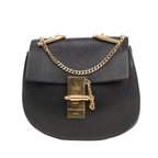 Black Chloé Drew grained leather crossbody bag with gold-tone chain strap, flap front, and large gold-tone turn-lock clasp, front view on white background.