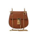 Front view of a brown Chloé Drew pebbled leather crossbody bag with a rounded shape, gold-tone clasp and chain shoulder strap.
