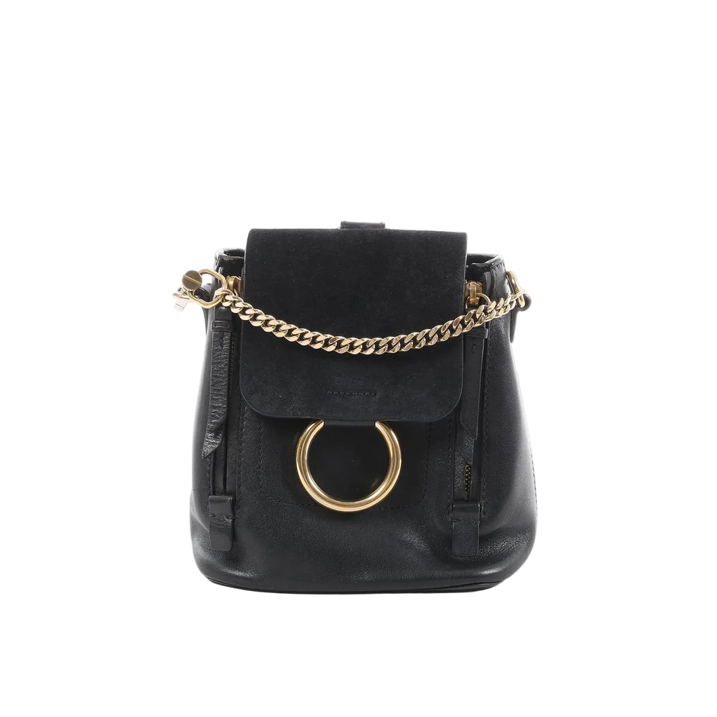 Chloé Faye black leather and suede backpack with gold-tone chain detail and large gold ring on front flap, front view on white background.