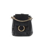 Chloé Faye black leather and suede backpack with gold-tone chain detail and large gold ring on front flap, front view on white background.
