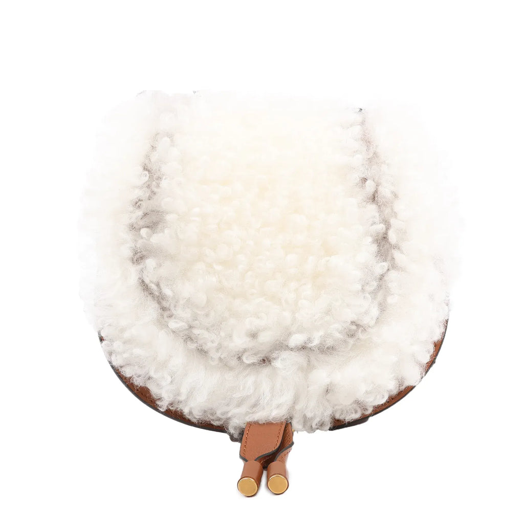 Chloé Marcie Mini Crossbody Bag in brown leather with a fluffy white boa shearling flap, curved saddle shape, and thin adjustable shoulder strap, shown against a white background.