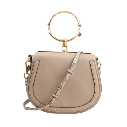 Chloé Nile Small 2Way Shoulder Bag in beige leather with gold-tone metal ring handle, adjustable crossbody strap, and curved saddle silhouette on a white background.
