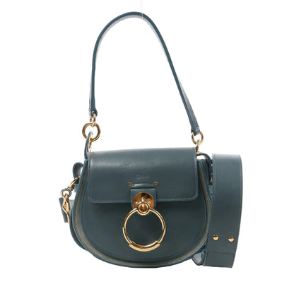 Front view of the Chloé Tess Small Leather 2Way Handbag in blue, showcasing a rounded saddle-style silhouette, gold-tone oversized ring detail on the flap, top handle, detachable shoulder strap, and smooth leather finish, displayed against a white background.