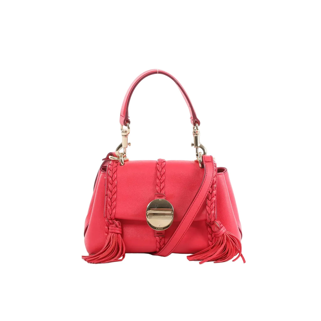 Chloé Penelope pink leather handbag with top handle, braided trim, gold-tone round clasp, tassel accents, and detachable shoulder strap, front view on white background.