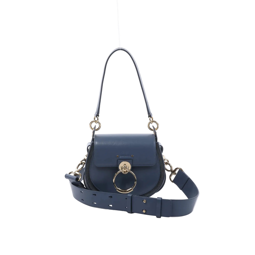 Chloé Tess Small blue leather 2-way shoulder bag with flap closure, large gold ring hardware, top handle, and wide adjustable strap on white background.
