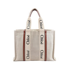 Chloé Woody Large tote bag in beige canvas with brown leather trim, black logo webbing handles, and an open-top design displayed on a white background.