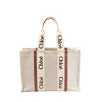 Chloé Woody Large beige canvas tote with brown leather trim and wide logo webbing straps, front view on white background.