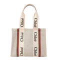 Chloé Woody Medium Tote Bag in beige canvas with brown leather side trim and bold ivory logo-printed fabric shoulder straps.