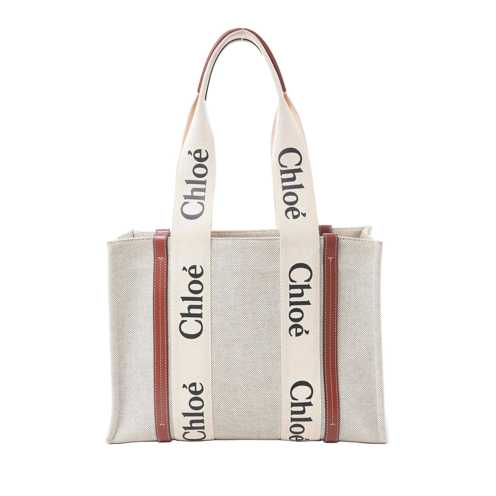 Chloé Woody Medium beige canvas tote bag with brown leather trim, wide logo shoulder straps, and structured open-top shape on white background.