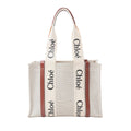 Chloé Woody Medium beige canvas tote bag with brown leather trim, wide logo shoulder straps, and structured open-top shape on white background.