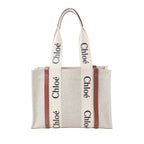 Chloé Woody Medium beige canvas tote bag with brown leather trim, wide logo shoulder straps, and structured open-top shape on white background.