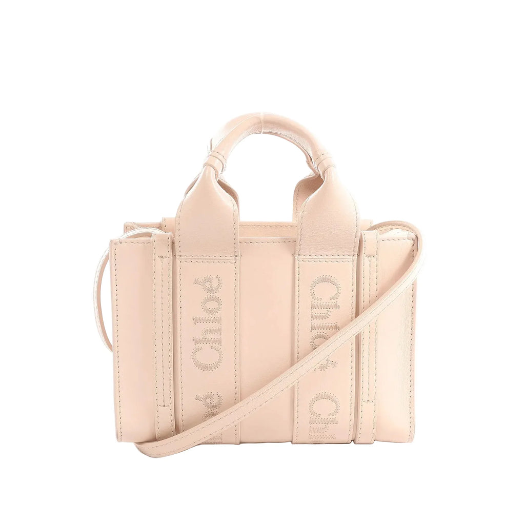 Blush pink Chloé Woody Mini leather handbag with top handles, tonal logo webbing straps, and a slim crossbody strap.