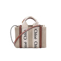 Front view of Chloé Woody Nano tote in beige canvas with vertical “Chloé” logo webbing, brown leather trim, top handles, and a brown leather shoulder strap.