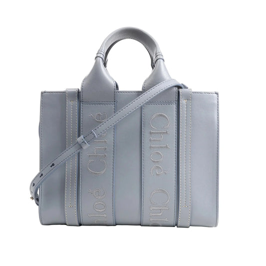 Chloé Woody Small 2Way Handbag in blue leather featuring logo-embroidered vertical straps, top handles, adjustable shoulder strap, and structured rectangular silhouette, displayed on a white background.