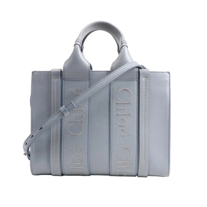 Chloé Woody Small 2Way Handbag in blue leather featuring logo-embroidered vertical straps, top handles, adjustable shoulder strap, and structured rectangular silhouette, displayed on a white background.