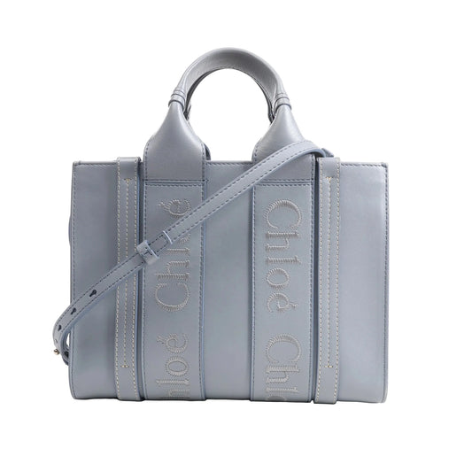 Chloé Woody Small 2Way Handbag in blue leather featuring logo-embroidered vertical straps, top handles, adjustable shoulder strap, and structured rectangular silhouette, displayed on a white background.