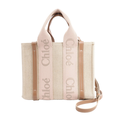 Chloé Woody Small handbag in beige canvas with light brown leather trim, dual logo-printed top handles, and detachable shoulder strap against a white background.