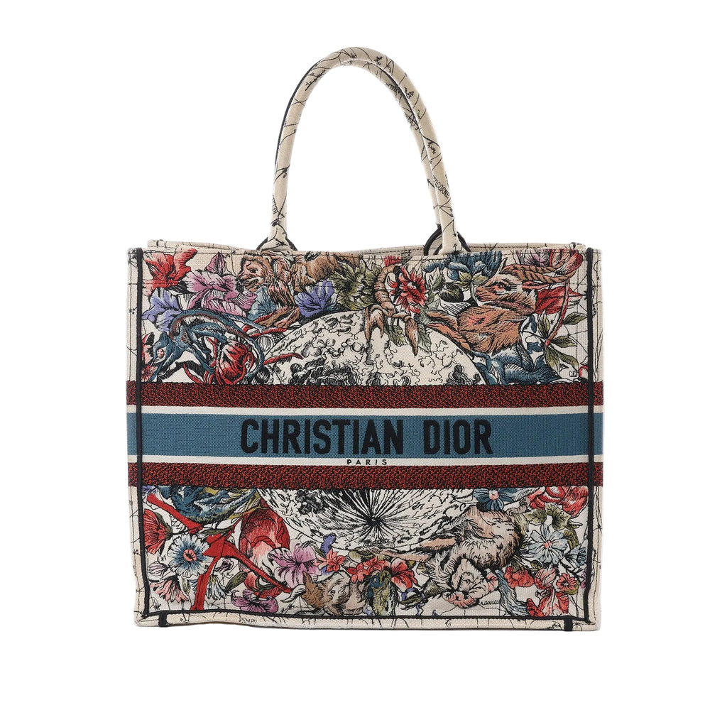 Front view of Dior Book Tote Large in multicolor zodiac print canvas with top handles, floral and animal illustration, and blue band reading “CHRISTIAN DIOR PARIS.”