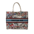 Front view of Dior Book Tote Large in multicolor zodiac print canvas with top handles, floral and animal illustration, and blue band reading “CHRISTIAN DIOR PARIS.”