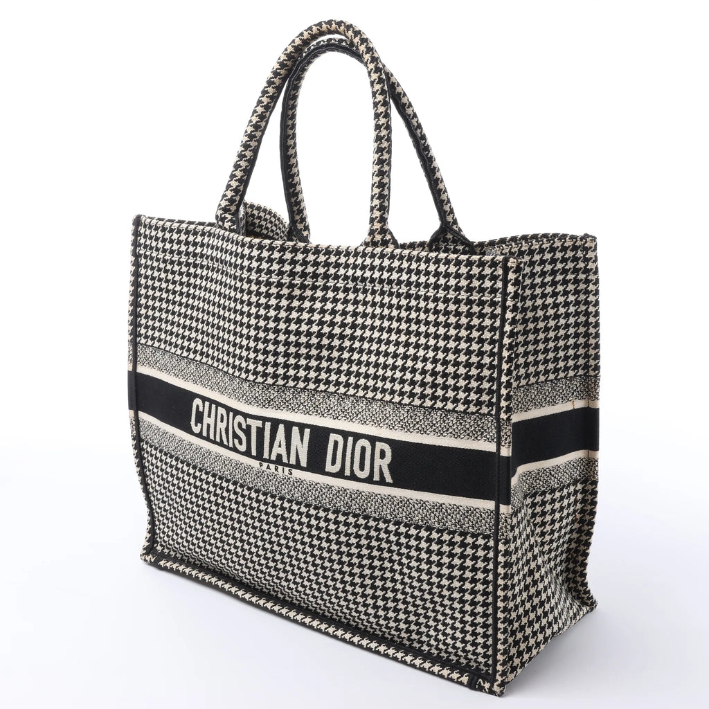 Angled front view of a large black and white Dior Book Tote with a houndstooth pattern, dual handles and Christian Dior logo band.