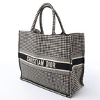 Angled front view of a large black and white Dior Book Tote with a houndstooth pattern, dual handles and Christian Dior logo band.