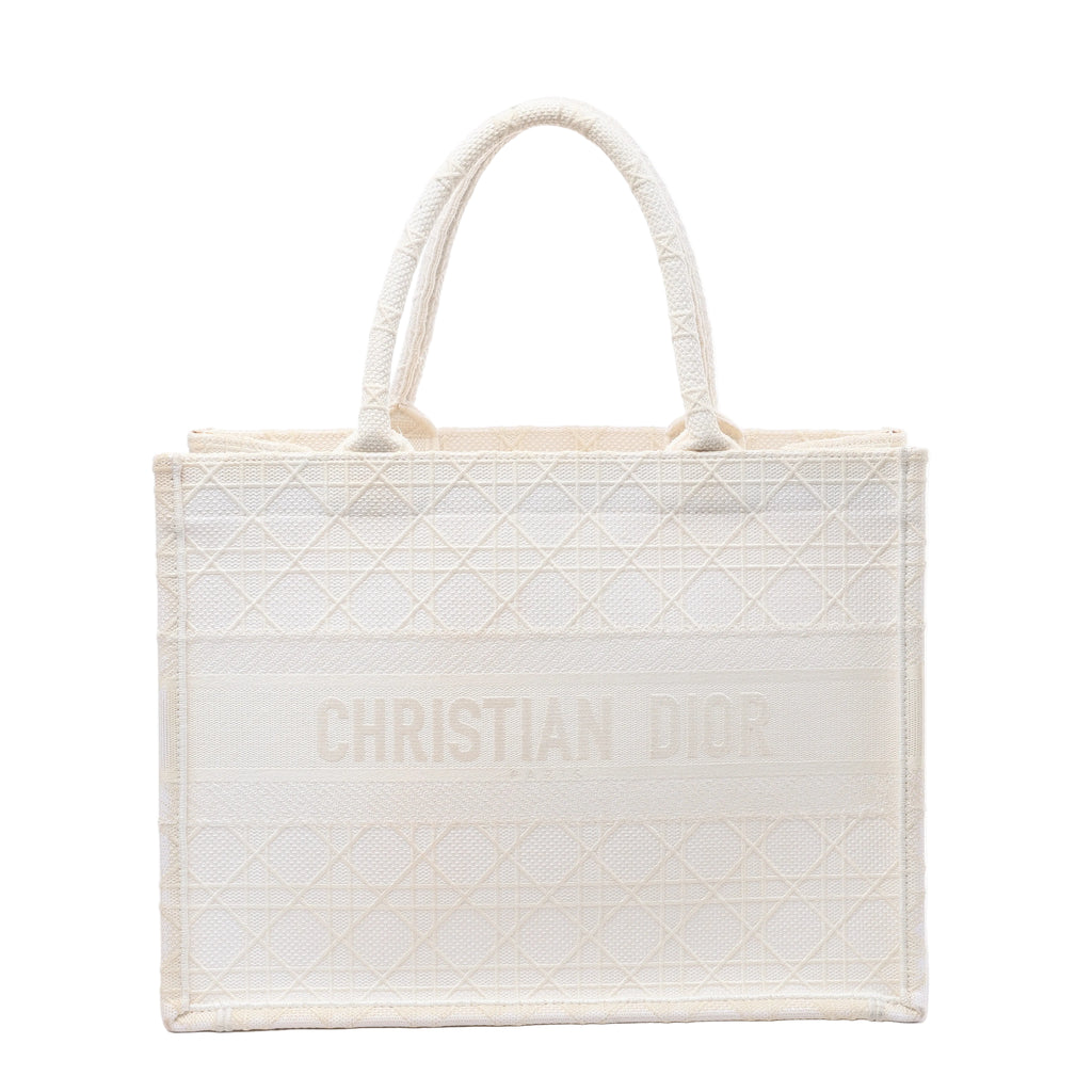 White Christian Dior Book Tote Medium canvas bag with tonal geometric embroidery, dual top handles and CHRISTIAN DIOR lettering across the front.