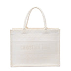 White Christian Dior Book Tote Medium canvas bag with tonal geometric embroidery, dual top handles and CHRISTIAN DIOR lettering across the front.