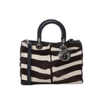 Dior Diorissimo 2-way handbag in brown and white zebra-print haircalf with black leather top handles, detachable strap, silver-tone hardware, and hanging DIOR letter charms on white background.