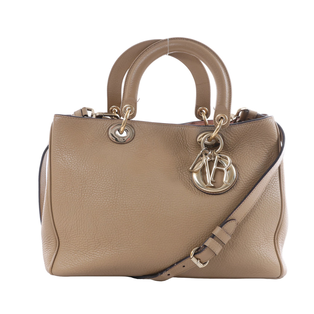 Beige Christian Dior Diorissimo leather handbag with rounded top handles, shoulder strap, gold-tone hardware and hanging DIOR letter charms on a white background.
