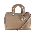 Beige Christian Dior Diorissimo leather handbag with rounded top handles, shoulder strap, gold-tone hardware and hanging DIOR letter charms on a white background.