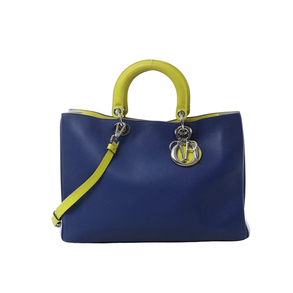Dior Diorissimo large navy blue leather handbag with yellow top handles, yellow shoulder strap, and silver-tone DIOR letter charms on white background.