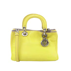 Dior Diorissimo mini yellow leather handbag with rounded top handles, detachable shoulder strap, and silver-tone DIOR letter charms on a white background.