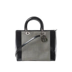 Dior Lady Dior handbag with black patent leather sides and handles, black-and-white canvas panel, silver-tone hardware, and hanging Dior letter charms.