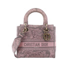 Dior Lady D-Lite Medium pink Toile de Jouy embroidered canvas handbag with top handles, shoulder strap, CHRISTIAN DIOR front logo, and gold-tone DIOR charms on white background.