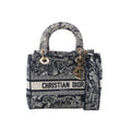 Dior Lady D-Lite Medium handbag in navy blue and white embroidered canvas with Christian Dior logo band, gold-tone DIOR charms, top handles and detachable shoulder strap on white background.
