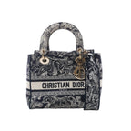 Dior Lady D-Lite Medium handbag in navy blue and white embroidered canvas with Christian Dior logo band, gold-tone DIOR charms, top handles and detachable shoulder strap on white background.