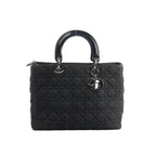 Front view of Dior Lady Dior Large handbag in black Cannage quilted denim with glossy black top handles, silver-tone hardware, and hanging DIOR letter charms.