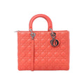 Dior Lady Dior large orange leather handbag with Cannage quilting, rounded top handles, silver-tone hardware, hanging Dior charms, and shoulder strap on a white background.