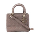 Front view of a medium beige Dior Lady Dior Cannage leather handbag with rounded top handles, gold-tone D.I.O.R. charms and a shoulder strap.