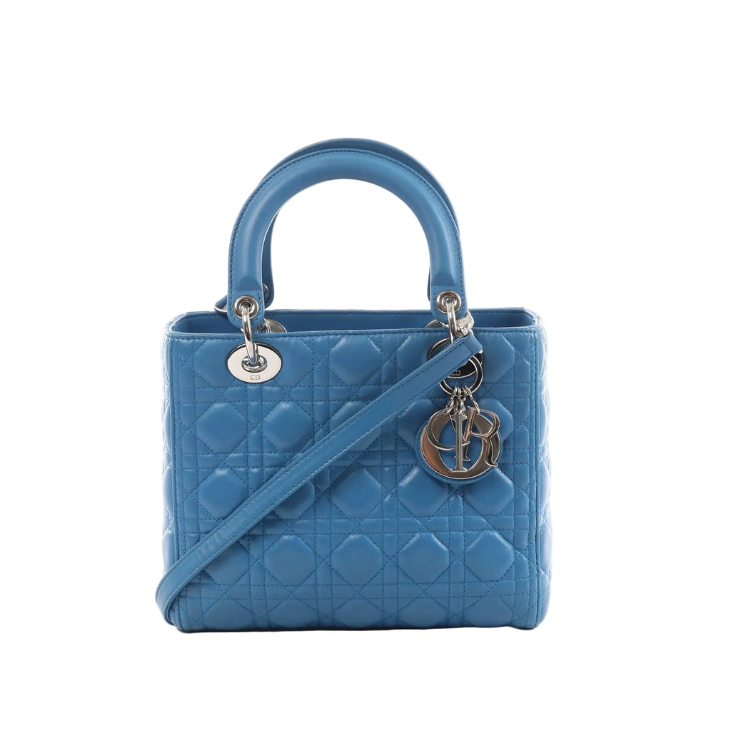 Blue quilted leather top-handle handbag with cannage stitching, detachable shoulder strap, silver-tone hardware, and dangling Dior letter charm on a white background.