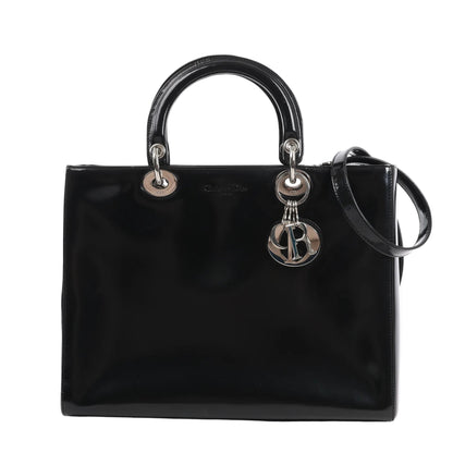 Dior Lady Dior large 2Way handbag in glossy black patent leather with silver hardware, dual rounded top handles, detachable shoulder strap, and dangling 'D.I.O.R.' logo charms, displayed against a white background.