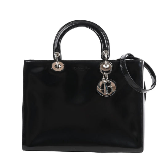 Dior Lady Dior large 2Way handbag in glossy black patent leather with silver hardware, dual rounded top handles, detachable shoulder strap, and dangling 'D.I.O.R.' logo charms, displayed against a white background.