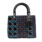 Front view of a Dior Lady Dior Medium Handbag in navy blue, embellished with orange, blue, and black sequins in geometric patterns, featuring black leather handles, silver-tone hardware, and hanging Dior letter charms, displayed against a white background.