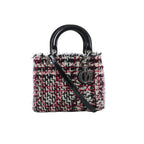 Dior Lady Dior Small handbag in black, white, and red tweed with glossy black top handles, black patent leather shoulder strap, and silver-tone DIOR charms on white background.