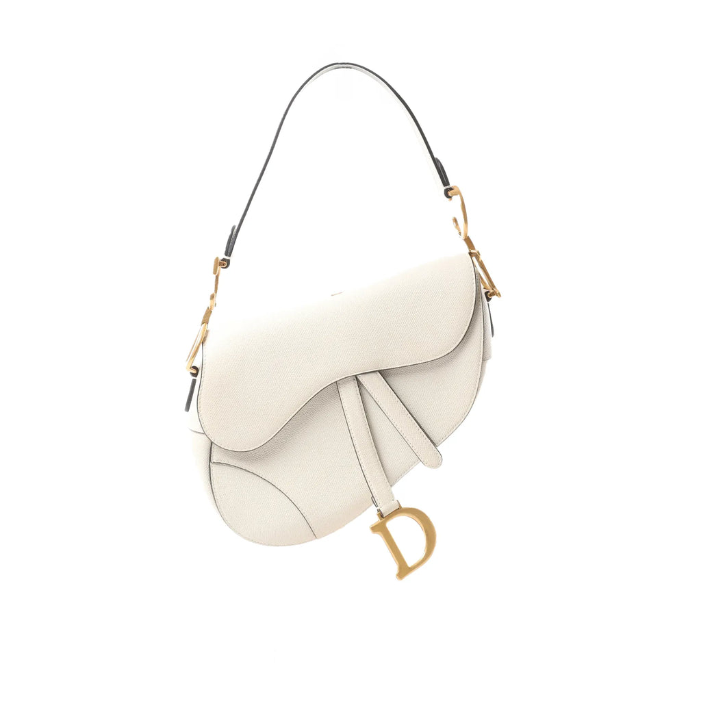 White Dior Saddle shoulder bag with curved flap, adjustable strap, and large gold-tone D charm hanging at the side