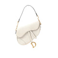 White Dior Saddle shoulder bag with curved flap, adjustable strap, and large gold-tone D charm hanging at the side