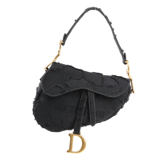 Dior Saddle Classic Bag in black canvas with tonal embroidered detailing, short shoulder strap, and antique gold ‘D’ charm hanging from the flap on a white background.