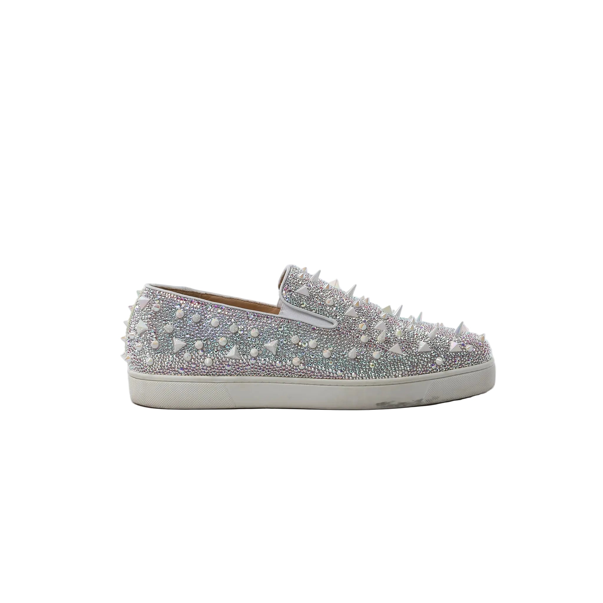 White Christian Louboutin slip-on sneaker covered in clear Swarovski crystals with white spike studs and white rubber sole, side view on white background